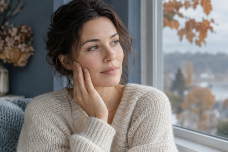 Frau im Strickpullover bei der Hautpflege an einem herbstlichen Fenster